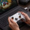 02-l Person holding a white game controller over a laptop keyboard with a colorful game on the screen behind it.