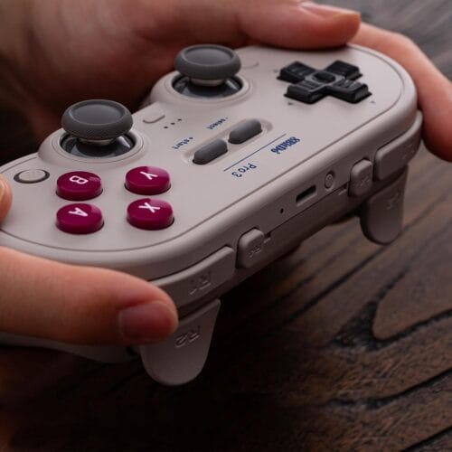 618EEbwlfWL._SL1500_ Close-up of a game controller being held, showing pink A B X Y buttons and gray analog sticks.