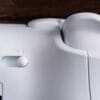 Version 1.0.0 Close-up of a white sewing machine highlighting a round control knob and the spool/bobbin area, with a wood surface in the background.