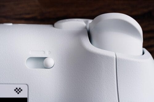 Version 1.0.0 Close-up of a white sewing machine highlighting a round control knob and the spool/bobbin area, with a wood surface in the background.