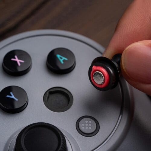 61HikWYNk2L._SL1500_ Close-up of a hand inserting a wireless earbud into a circular game controller with colorful X and A buttons.