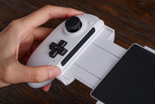 Version 1.0.0 Close-up of a white handheld game controller attachment held in a left hand, showing a black joystick and D-pad.