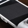 Version 1.0.0 Close-up of a white handheld game console with a large black textured touchpad on a wooden surface.