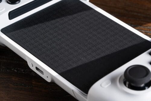 Version 1.0.0 Close-up of a white handheld game console with a large black textured touchpad on a wooden surface.