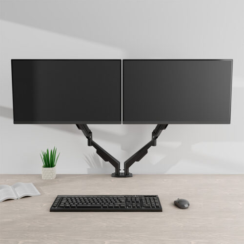 Dual-monitor setup on a desk with mounted arms, a keyboard, mouse, plant, and an open book on the left.