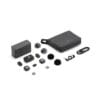 DJI camera accessories scattered on a white background: carrying case, charger, wireless transmitter, mics with windshields, cables and small accessories.