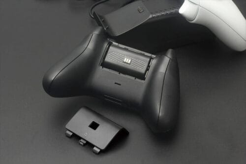 next-accessories-xbox-NXXCHRG2-54190026-1-1024x683 Black wireless game controller with a removable battery pack and charging dock on a dark surface, controller shown from the top/side view with battery slot open.