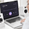 Laptop displaying a music player interface with play button, flanked by white speakers on a desk.