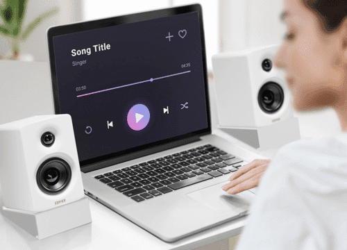 Laptop displaying a music player interface with play button, flanked by white speakers on a desk.